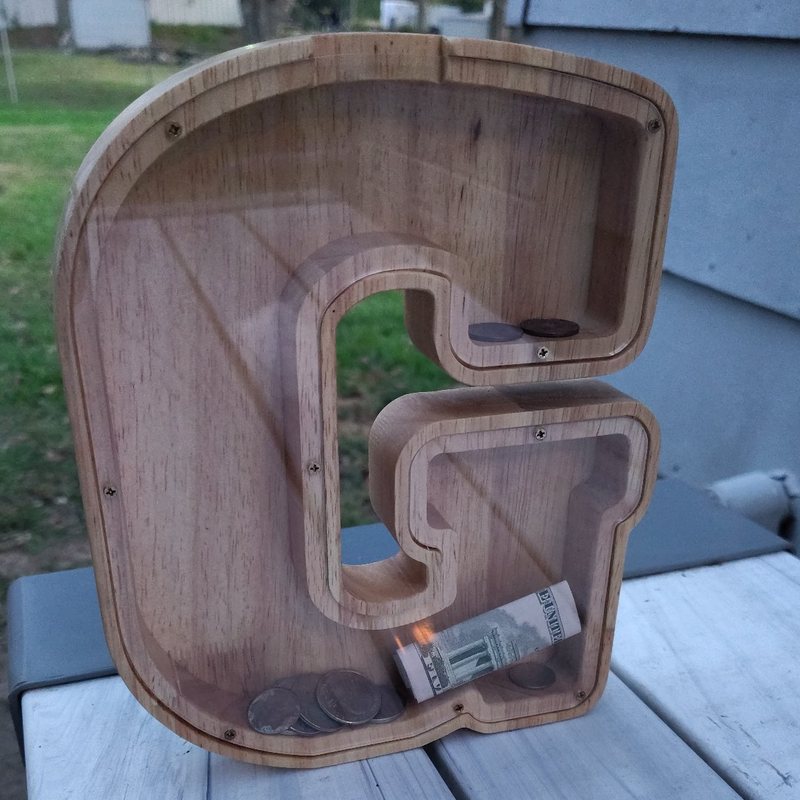 Alcancía de letras de madera SumiDate — una alcancía de madera en forma de letra G con ventana transparente, monedas y un billete doblado adentro